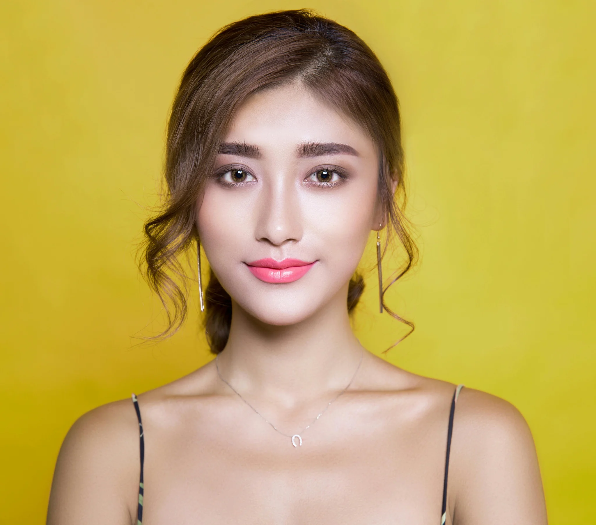 A woman with long hair and a smile stands against a bright yellow background, wearing a sleeveless top.