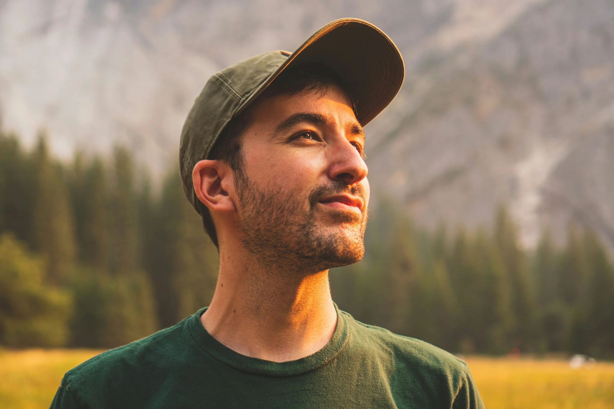 Man in a green cap and shirt looks up towards the sun with a happy expression.