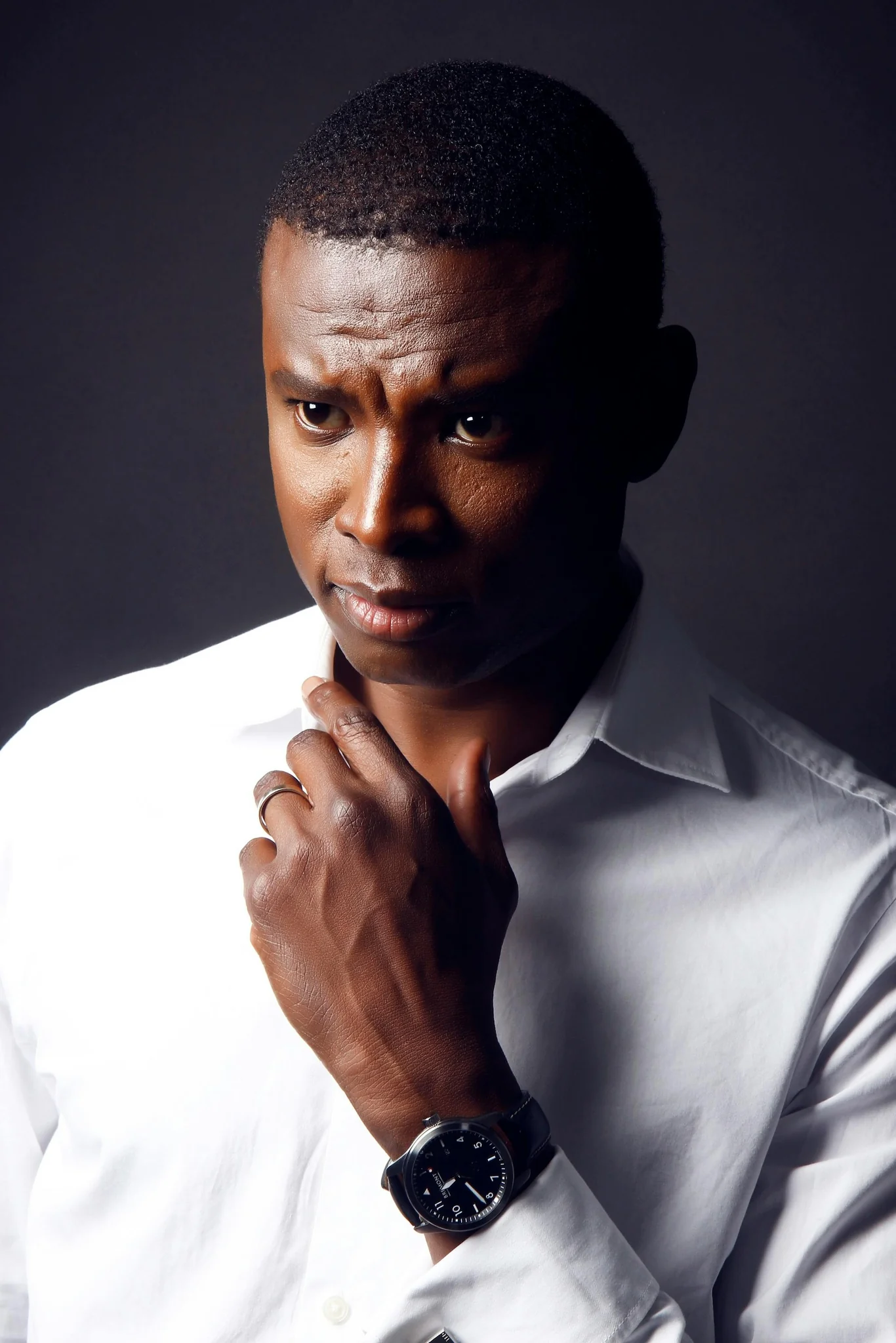 Portrait of a Black man in a white button-down shirt looking thoughtful. He's wearing a watch and has short hair.